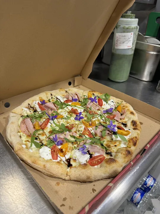 Pizza garnie de roquette et de fleurs comestibles sur une planche